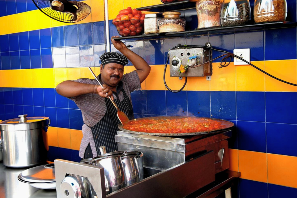 Pav bhaji being cooked on a large griddle at a Mumbai food stall.